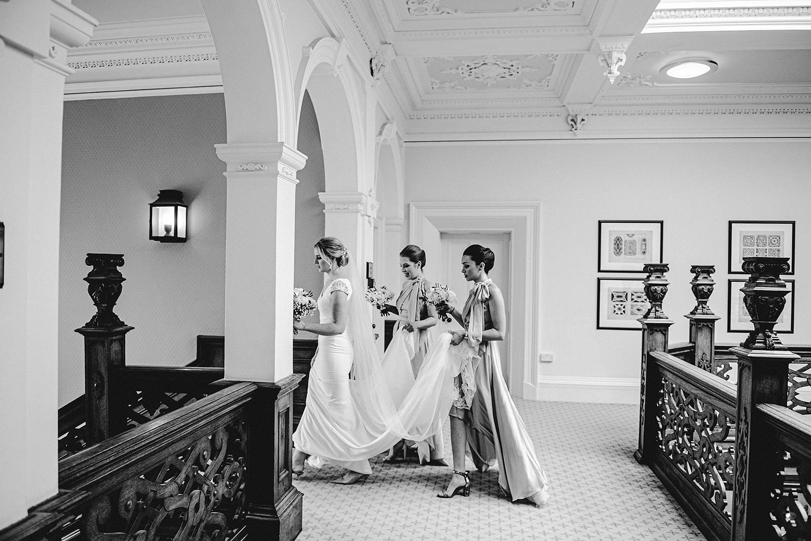 bride walking down the satirs to her ceremony with her bridesmaids holding her dress at Babbighton house on somerset