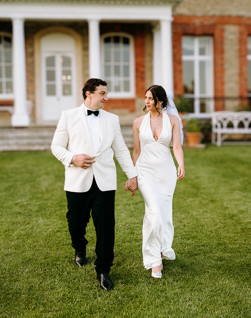 Bride and grrom walking toether with the wedding venue in the background at Ardington House.