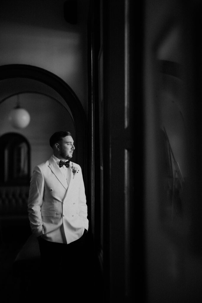 A black and white image of a groom next tio the window at The Roman Baths in Bath, Somerset