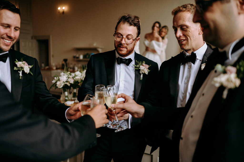 Group of groomsmen in tuxedos clinking champagne flutes in a wedding toast. Andrew Brannan Photography