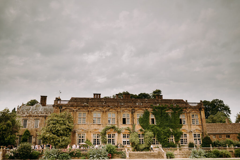 Historic stone manor with ivy-covered walls and a formal garden; gray, cloudy sky above and visitors on the steps in the foreground. Andrew Brannan Photography