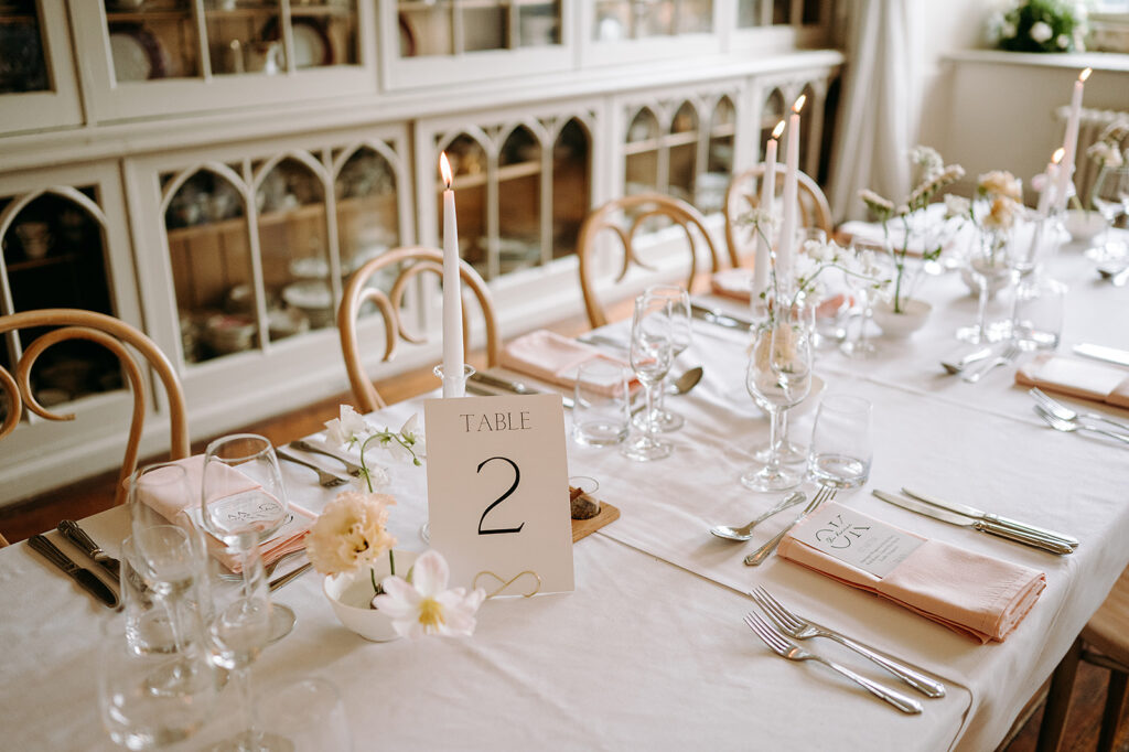 Elegant dining table set for a formal event with candles, pink napkins, and a table number card reading 'TABLE 2'. Andrew Brannan Photography