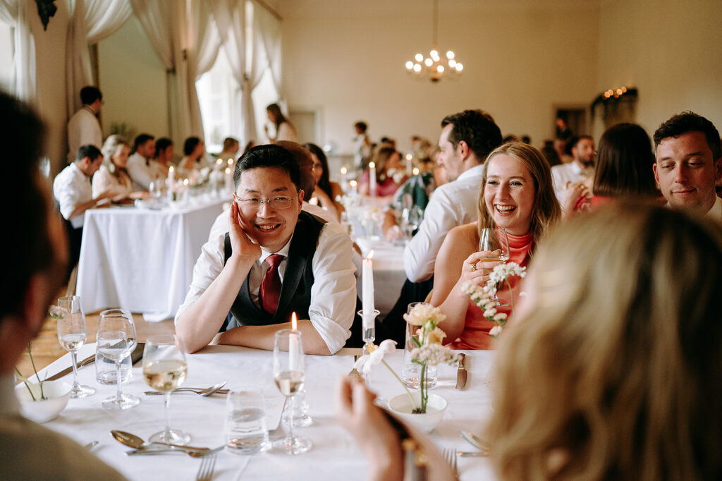 Guests seated at a candlelit wedding reception table, smiling and chatting. Andrew Brannan Photography