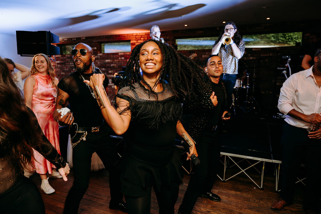 Group of people dancing at a lively party with a singer in the foreground and a band performing on a small stage behind them Andrew Brannan Photography